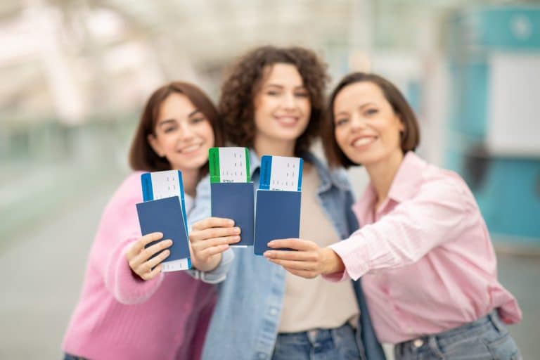 Three friends joyfully displaying their passports and tickets at the airport